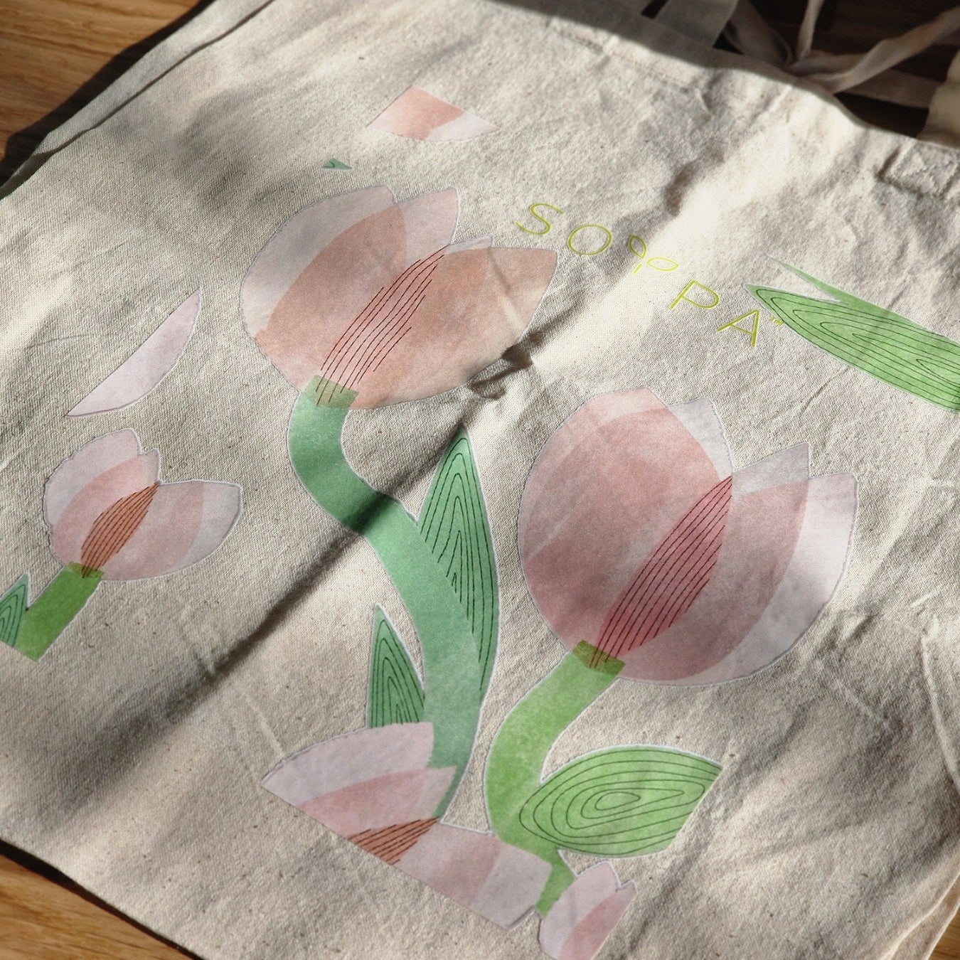A beige cotton tote shopping bag with a printed design featuring colorful houses and the brand name 'SOYPAA'.
